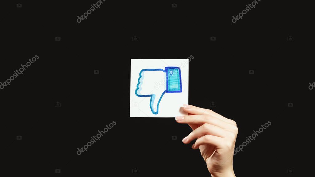 Kharkiv, Ukraine - May 12, 2020: Dislike icon. Negative feedback. Female hand showing disapproving Facebook thumb down sign isolated on dark black empty space background.