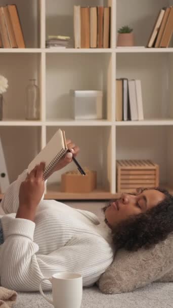 垂直录像 创意写作 女作家 家庭休闲 日记本中梦幻般的女性计划享受在房间地板舒适的垫子上的放松 — 图库视频影像