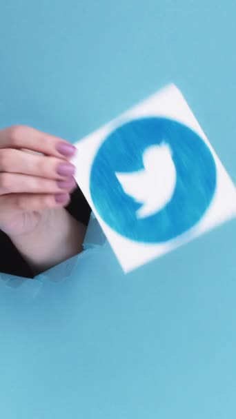 ハリコフ ウクライナ 2020年6月4日 垂直ビデオ Twitterのアイコン ソーシャルメディア 女性ブロガー手内側画期的な紙の穴ショーモバイルアプリのロゴ上の青引き裂かれた背景 — ストック動画