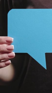Dikey video. Diyalog simgesi. Çevrimiçi iletişim. Koyu boşluk arkaplan üzerinde ileti metni için mavi boş konuşma baloncuğu gösteren kadın el.