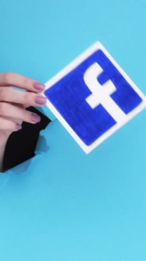 Kharkiv, Ukrayna - Haziran 04, 2020: Dikey video. Facebook ikonu. Sosyal medya. Kırık mavi arkaplanda uygulama işareti gösteren kağıt deliğinin içindeki kadın eli.