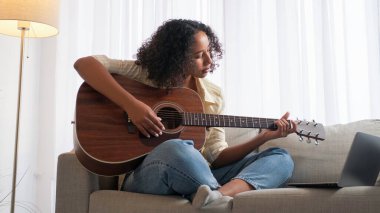 İnternetten ders. Gitar eğitimi. Ev tatili. Mutlu kadın dizüstü bilgisayarda telli çalgılar öğreniyor. Koltuk lambası odasında akorlar çalışıyor..