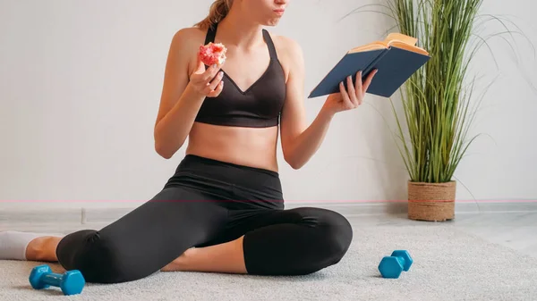 ダイエット研究 フィットネス栄養 ジャンクフードのカロリー 運動能力のない女性読書本を食べる甘いドーナツデザートで床にダンベルオンライトフリースペース — ストック写真