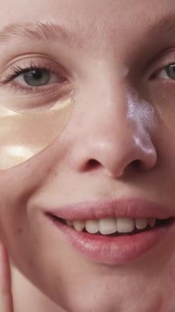 垂直录像 眼斑美容品皮肤治疗 用金黄色胶原水胶面膜触摸洁白容光焕发的脸上的满意微笑女人的面容 — 图库视频影像
