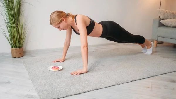 フィットネスの動機 減量の食事療法 カロリーが燃焼する 自信に満ちた運動女が甘いドーナツデザートと床の上でプッシュアップ運動を行う — ストック写真