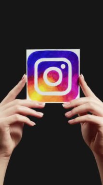 Kharkiv, Ukrayna - 12 Mayıs 2020: Dikey video. Instagram 'ı takip et. Küresel iletişim Sosyal medya uygulama simgesini tutan kadın eller koyu boş alan arkaplan döngüsünde izole edilmiş.