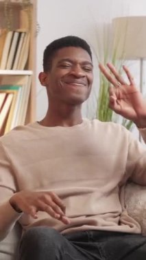 Dikey video. Onaylandı. Tamam jest. Memnuniyet verici genç adam evdeki oturma odasındaki kanepede tavsiye yazısı gösteriyor..