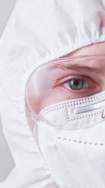 Dikey video. Tıp bilimcisi. Covid-19 salgını. Beyaz koruyucu ekipmanlı kadın doktor maske gözlükleri tüm kaputta..