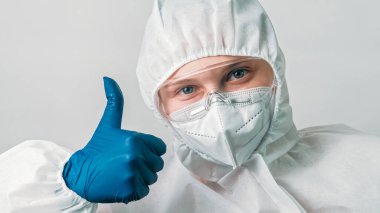 Sağlık bilimcisi. Tıbbi yardım. İyi niyet göstergesi. Virüs enfeksiyonu koruma ekipmanı içinde kadın doktor. Gri arka planda el işareti gibi onaylı..