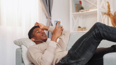 Müzik dinliyordum. Şarkı molası. Ses aygıtı. Rahatlamış genç adam evde oturma odasındaki kanepede dinlenen kulaklıklarıyla favori müzik listesinin keyfini çıkarıyor..