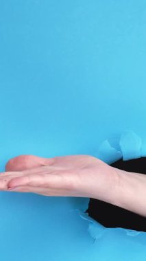 Dikey video. Reklamcı el. Sunum jesti. Kadın avucunun içi açık, delinme deliği mavi yırtık duvar zemininde, boş arkaplanı olan bir şey gösteriyor..