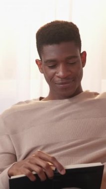 Dikey video. Roman okuyorum. Edebiyat hobisi. Ev tatili. Keyifli ve rahat genç adam ilginç kağıt çok satanlar kitabında dinleniyor..