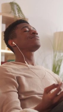 Dikey video. Ev meditasyonu. Yoga sakinliği. Ses rahatla. Rahatlık ve rahatlık. Huzurlu sakin adam oturma odasındaki koltukta kulaklıkla müzik dinliyor..