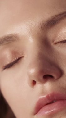 Dikey video. Kadın yüz bakımı. Yumuşak ten. Uçan saçlarıyla, pürüzsüz nemlendirilmiş parlak yüzlü çıplak omuzlara dokunan genç, doğal güzel bir kadın..