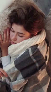 Dikey video. Hapşırma belirtileri. Mevsimsel grip. Hasta kadın kanepede yatarken soğuk algınlığı geçiriyor. Evde burun nezlesi geçiriyor..