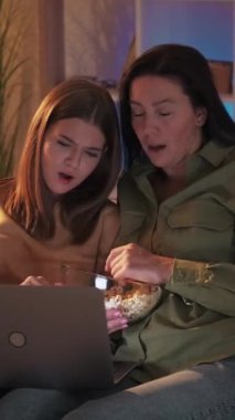 Dikey video. Korku izlemesi. İnternet filmi. Korkak genç kız dizüstü bilgisayarında patlamış mısır kasesiyle gerilim filmi seyrediyor..