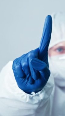 Dikey video. Doktor uyarısı. Sağlık uzmanıyım. Koruyucu ekipman maskeli kadın virüs uzmanı eldivenler gri arka planda el işaretini durdurdu.