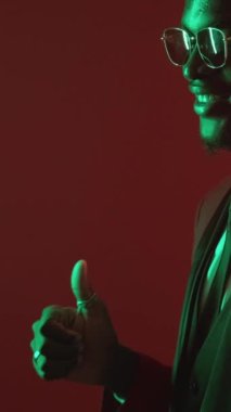 Dikey video. Cesaret verici bir jest. İyi iş çıkardın. Onaylanmış bir hayranlık. Yeşil, neon ışıklı, zarif takım elbiseli adam baş parmağıyla işaret ederek saygı gösteriyor..