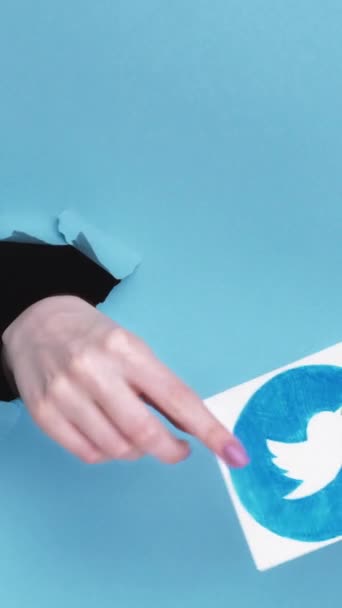 ハリコフ ウクライナ 2020年6月4日 垂直ビデオ Twitterのアイコン 女性加入者手で突破紙穴受け入れるソーシャルメディアアプリロゴ上の青引き裂かれた空のスペースの背景 — ストック動画