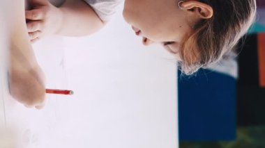 Dikey video. Sanat hobisi. Küçük kız. Resim yapmaktan zevk alıyorum. Beyaz kağıda kurşun kalemle çizim yapan kadın stüdyo içi hareket görüşünde..