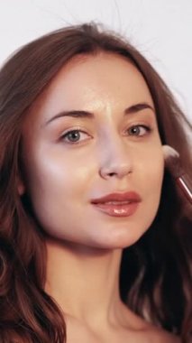 Dikey video. Günlük makyaj. Temeli uygula. Yüz hatları. Profesyonel bir yüz ifadesi. Kusursuz cildinde pudra fırçası olan genç bir kadın..