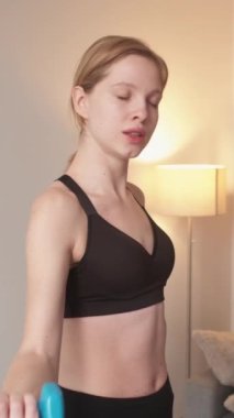 Dikey video. Yorucu bir spor. Ev antrenmanı. Güç kondisyonu. Halterleri kaldıran yorgun atletik kadın pazı kaslarını çalıştırıyor..