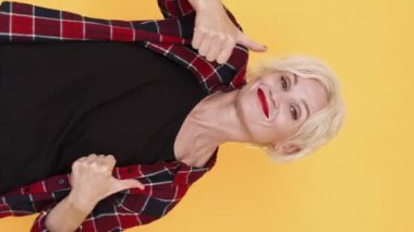 Dikey video. Birçok beğeni. Hareketli kadın. Neşeyi onaylıyorum. Mutlu orta yaşlı bayan baş parmak dansı yapıyor. Sarı üzerinde iyi hissediyor..