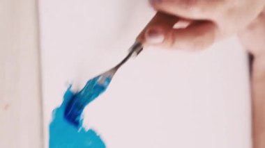Dikey video. Soyut resim. Boyama işlemi. Yaratıcı stüdyo. Tuvale spatula ve mavi boyalarla resim çizen tanınmayan bir kadın..
