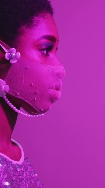 垂直ビデオ 顔のアクセサリー 隔離服だ 流行のパーティーだ 紫ピンク色ネオンライトプロフィールの自信満面の女性でメッシュマスク上の空の空間背景 — ストック動画