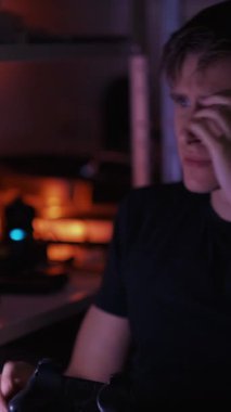 Dikey video. Oyuncu başarısız oldu. Çaresiz adam. Siber rekabet. Hayal kırıklığına uğramış bir adam bilgisayardaki oyunu kaybediyor. Karanlık ev içinde konsolu atıyor..