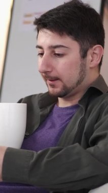 Dikey video. Telefon mesajlaşması. İnternet taraması. Gezici eğlence. Kahve fincanı olan mutlu bir adam cep telefonu sosyal medyasında sohbet ediyor..