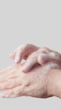 Dikey video. El hijyeni. Enfeksiyon önleme. Kadın avuçlarını ovuyor parmaklarını sabun köpüğüyle ovuyor beyaz arka planda izole edilmiş bakterilerden kurtuluyor..