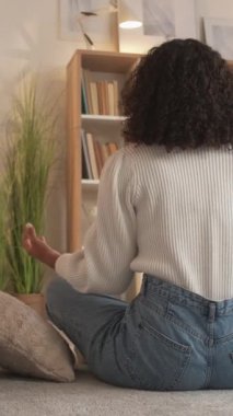 Dikey video. Meditasyon rahatla. Evde yoga. Sağlıklı bir yaşam. Huzurlu kadın oturma odasında yerde lotus pozu vererek nefes egzersizi yapıyor..