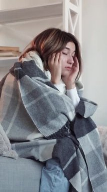 Dikey video. Baş ağrısı çekiyor. Hasta kadın. Bitkin düşmüş hasta kız ekoseli masaja sarılmış tapınaklarda kötü migren belirtileri yaşıyor..