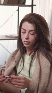Dikey video. Virüs hastalığı. Hasta kadın. Üşütürüm. Ekoseli kumaşı örten üzgün kadın hayal kırıklığı yaşıyor. İçerideki yüksek sıcaklığı görüyor..