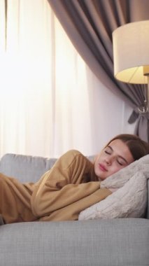 Dikey video. Uyku vakti. Anne bakımı. Haftasonu kanepede uyuyan ekoseli genç kızı örten sevgi dolu bir kadın..