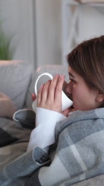 垂直录像 喉咙闷死了茶热 休息一下吧穿着毛毯热饮的冷冰冰的女人坐在家里明亮的沙发上 感到浑身冰凉 — 图库视频影像