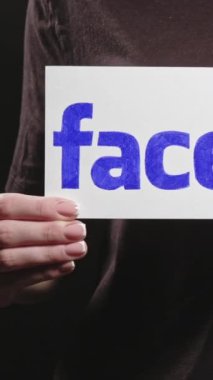 Kharkiv, Ukrayna - 12 Mayıs 2020: Dikey video. Facebook logosu. Sosyal medya tanıtımı. Koyu serbest alan arkaplanında uygulamayı tutan kadın..