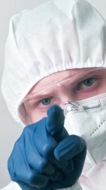 Dikey video. Tıp profesörü. Kızgın doktor. Eldivenli hemşire, gri arka planda parmak sallayarak uyarı işareti yapıyor..