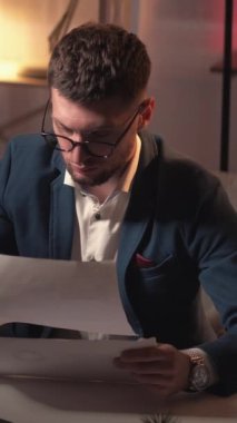 Dikey video. İş finansmanı. Çalışan adam. Bilgileri kontrol et Belgeler üzerinde çalışan zeki bir adam. Veri raporuyla karanlık odanın içinde oturuyor..