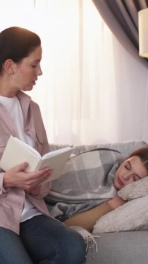 Dikey video. Aile okuması. Ebeveyn eğlencesi. Sevgi dolu anne, kitaptan uyuklayan genç kıza kadar ilginç bir hikaye anlatıyor..
