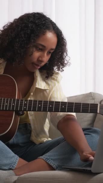 垂直ビデオ オンラインギターレッスン 音楽教育 ホームレジャー 陽気な女性Learningストリング楽器コースでラップトップ座ってソファでリビングルーム — ストック動画