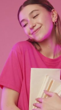 Dikey video. Edebiyat günü. Kitap festivali. Okuma hobisi. Pasifiğin pembe arka planında çok satan roman yığınıyla dans eden mutlu tatlı kadın..