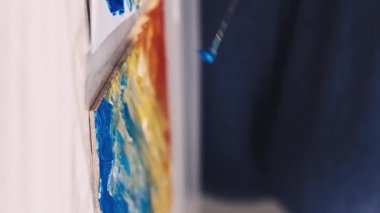 Dikey video. Sanat stüdyosu. - Kız öğrenci. Sanat eseri yaratımı. Tanımlanamayan bir kadın, renkli spatula resimleriyle tuvale soyut resim çiziyor..