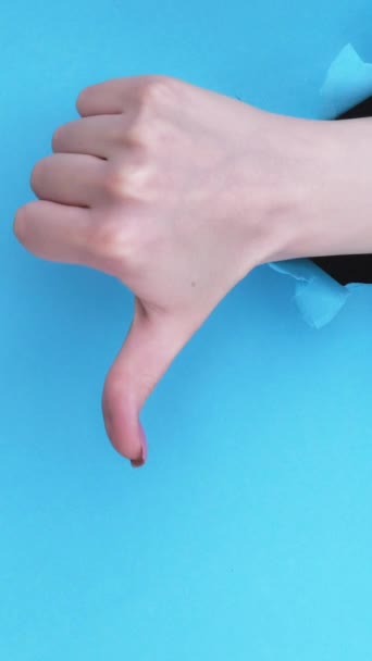 垂直录像 不喜欢的手势 负面反馈 蓝色撕破墙背景图上的突破纸孔中的雌性手显示拒绝拇指 复制空间设置为2圈 — 图库视频影像