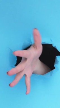 Dikey video. Şöyle böyle bir jest. Emin değilim. Şüpheci şüphe. Dişi el, mavi yırtık duvar zemininde yırtık kağıt deliğinin içinde el sallıyor..