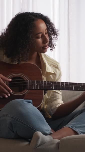 垂直ビデオ ギタープレイ学習 音楽研究 遠隔教育 勤勉な女性ギタリスト練習オンラインでノートパソコンでホームソファ — ストック動画