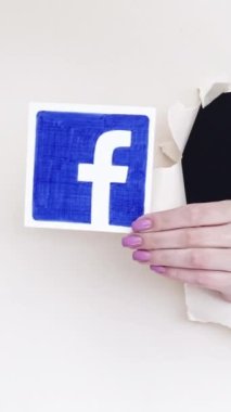 Kharkiv, Ukrayna - Haziran 04, 2020: Dikey video. Facebook ikonu. Sosyal medya. Beyaz boş arkaplanda uygulamayı gösteren bir kağıt deliğinin içindeki kadın eli.