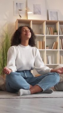 Dikey video. Ev meditasyonu. Yoga rahatla. Huzurlu sakin kadın oturma odasında yastıklarla lotus pozu veriyor..