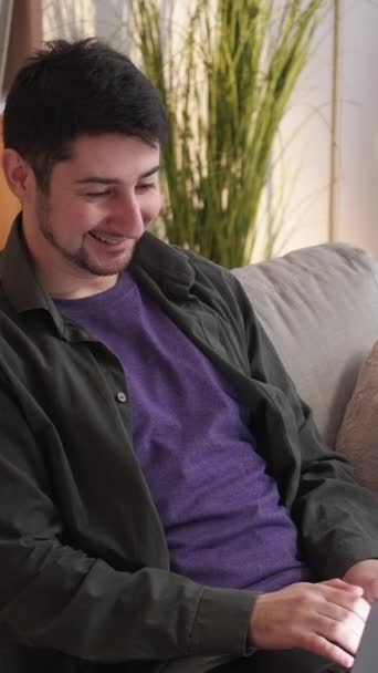 垂直ビデオ オンラインチャット ガジェット楽しい インターネットレジャー 楽しい笑顔男タイピングメッセージ上のラップトップブラウジングソーシャルメディア上の居心地の良いソファに家 — ストック動画
